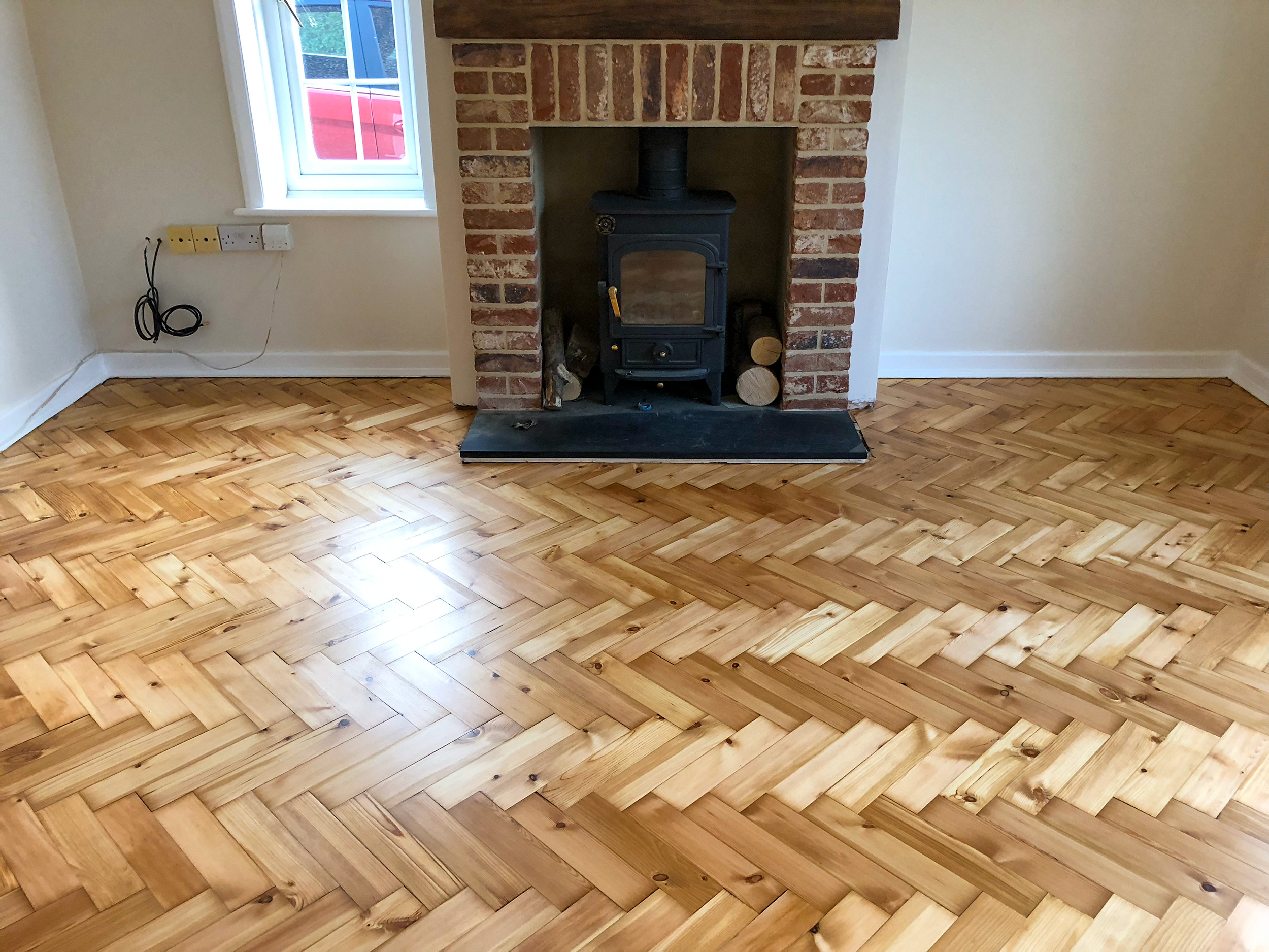 Sanded and refinished parquet floor restoration in living room with fireplace in background.
