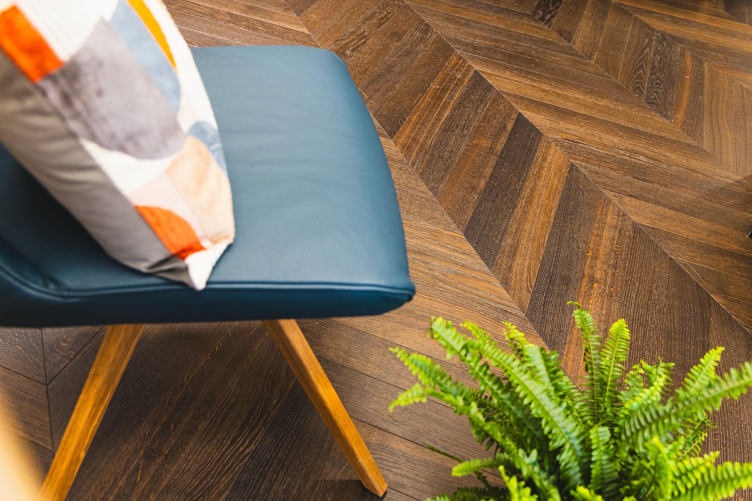 Artistic shot of dark toned parquet wood flooring with a blue chair and plant.