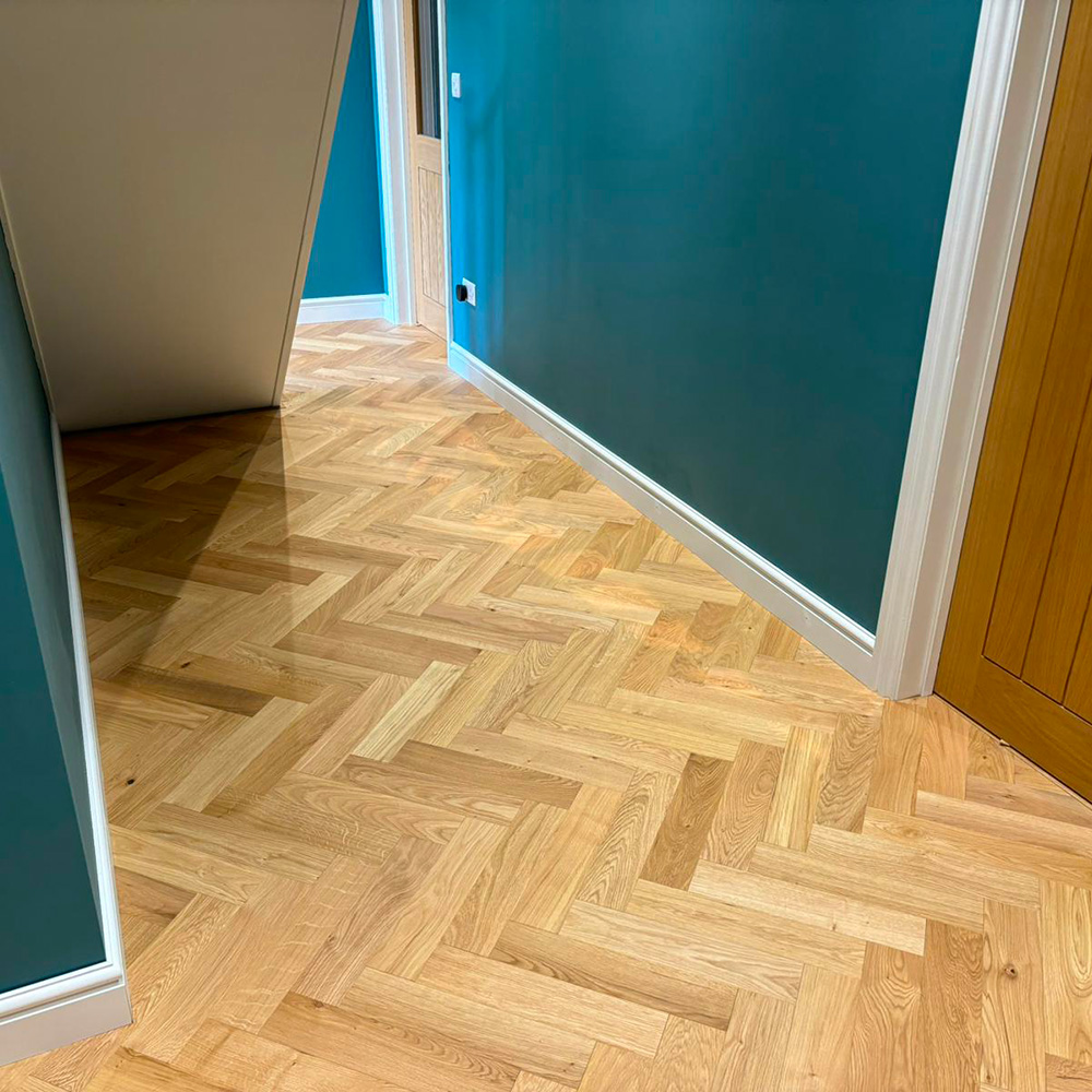 Lighter tone of oak herringbone parquet flooring in downstairs hall way with dark green walls.