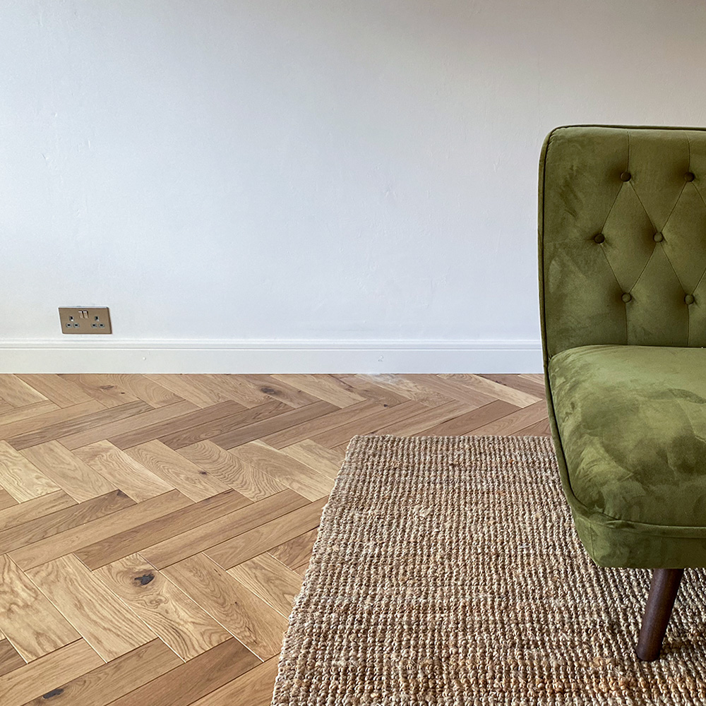 Parquet flooring supplied and fitting in a home with white walls part of green chair and small rug.