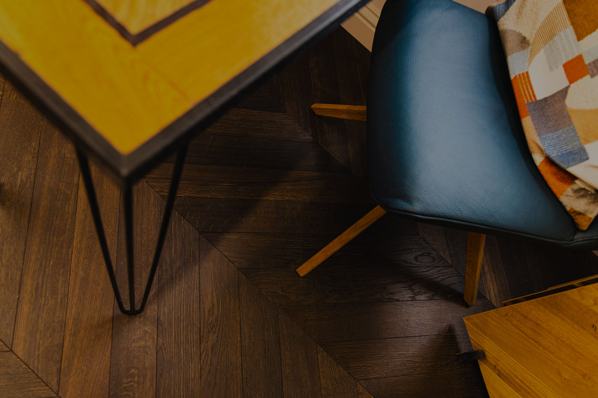 Stylish close up photo of a blue chair, table with a yellow top and dark colour wood flooring.