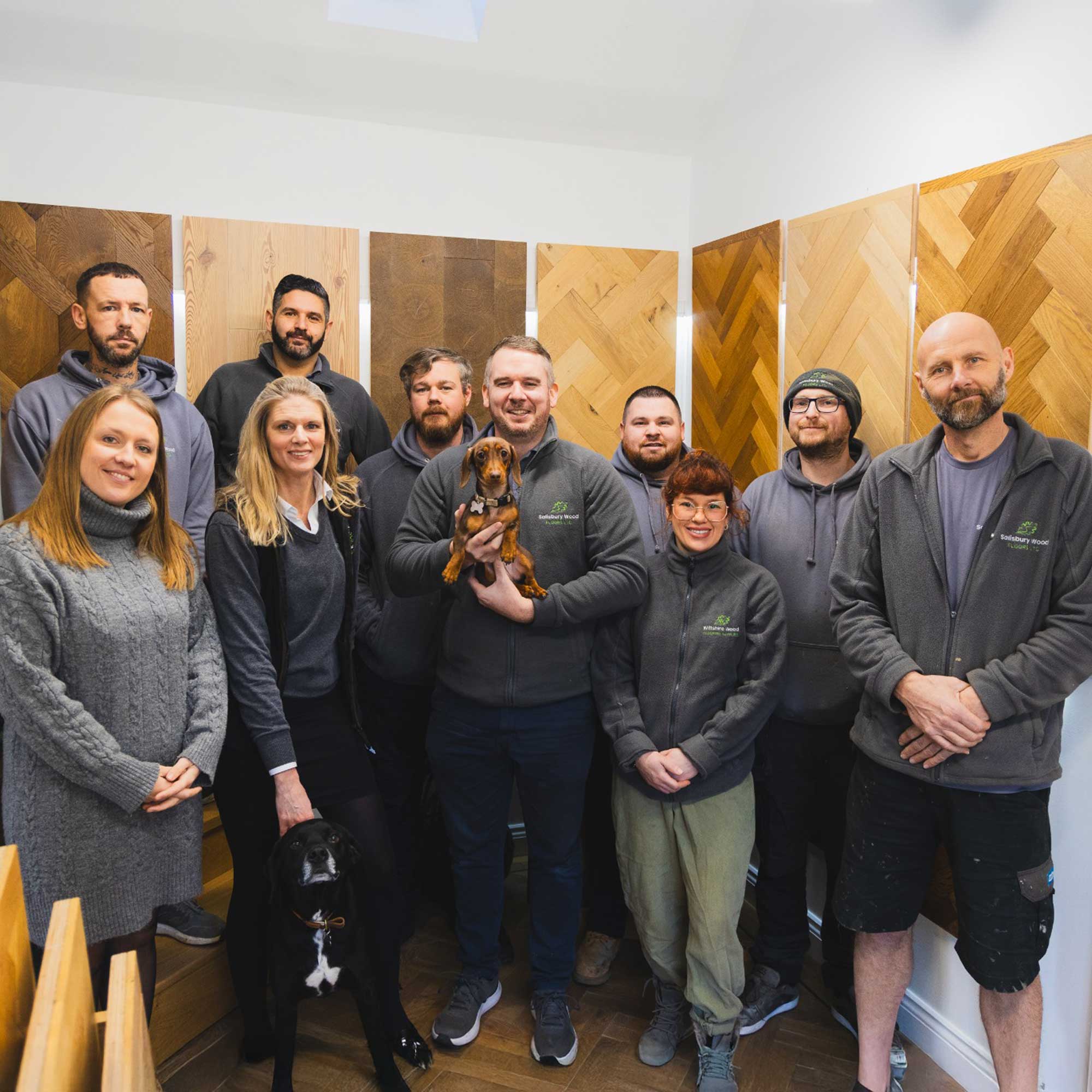 Salisbury wood floors team posing for a photo in front of some wood floor samples in their showroom.