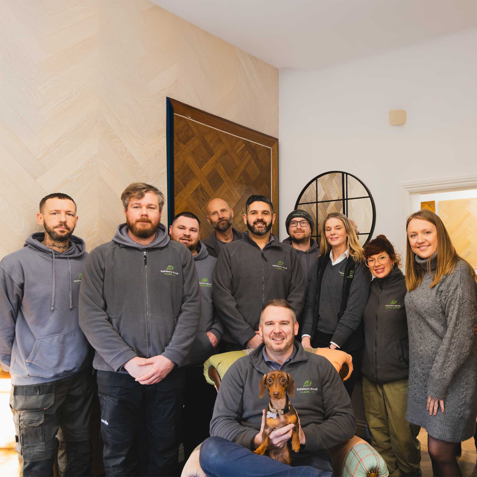 Salisbury wood floors team posing for a photo in their showroom with a small dog.