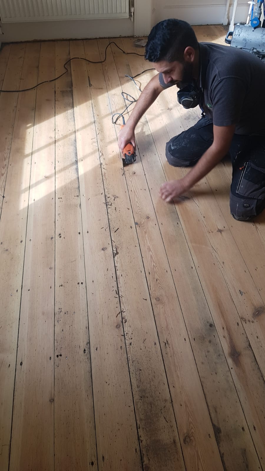 Man cleaning out joint on sanded wood floor.