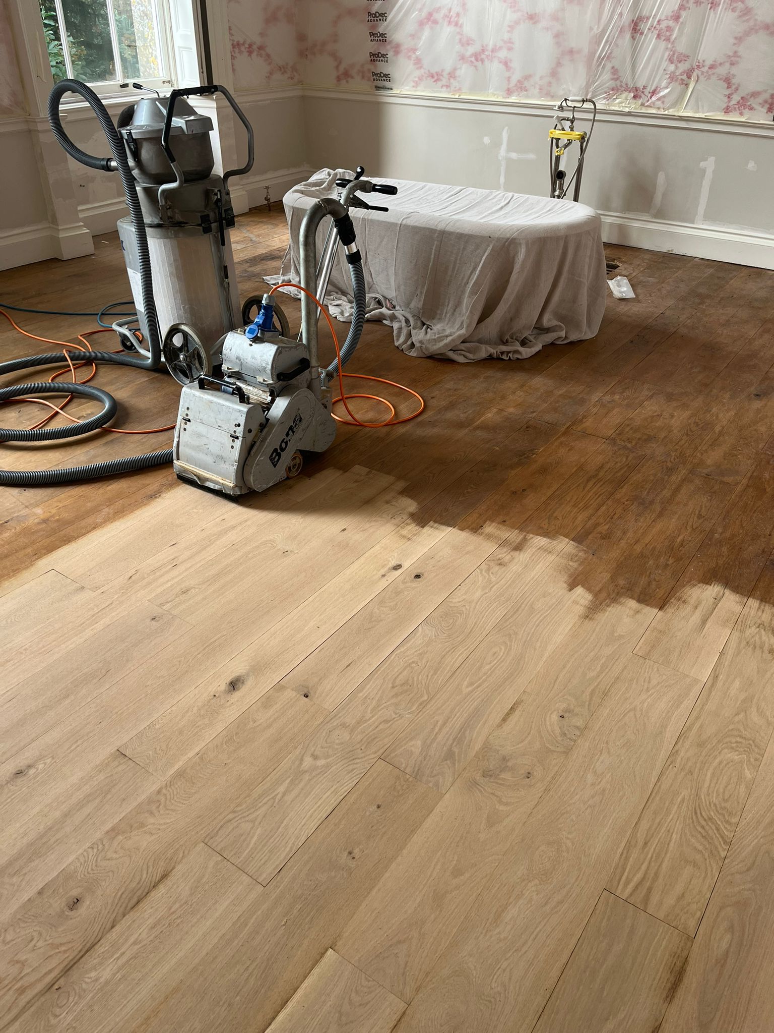 Bathroom wood floor in the process of being sanded by machinery.