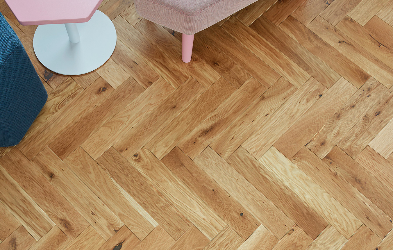 Herringbone wood floor pattern in room setting with a pink chair and lamp just about in view at the top.